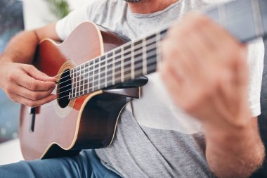 Adam oturma odasında akustik gitar çalıyor..