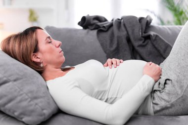 Pregnant tired exhausted woman with stomach issues at home on a 