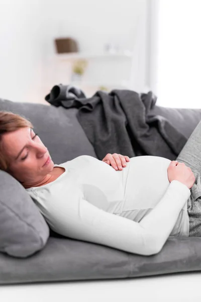 Pregnant tired exhausted woman with stomach issues at home on a — 스톡 사진