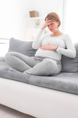Pregnant tired exhausted woman with stomach and head issues at h