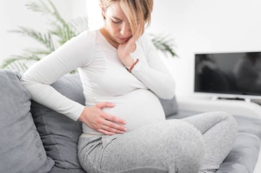 Pregnant tired exhausted woman with stomach and head issues at h