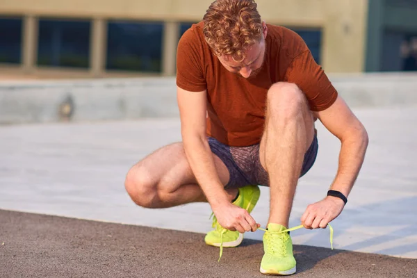 Joven hombre moderno atando zapatillas en un parque urbano . — Foto de Stock