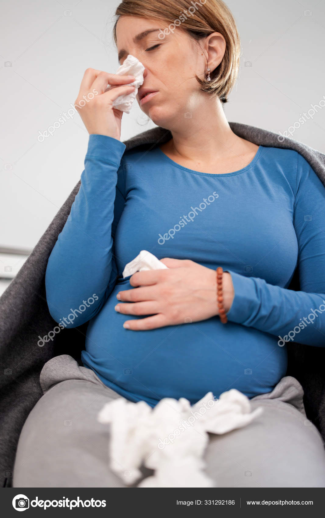 Pregnant woman catching cold, flu, virus, sitting at home on a c