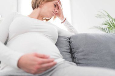 Pregnant tired exhausted woman with stomach and head issues at h