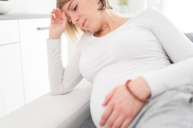Pregnant tired exhausted woman with stomach and head issues at h
