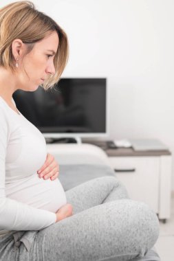 Pregnant tired exhausted woman with stomach issues at home on a 