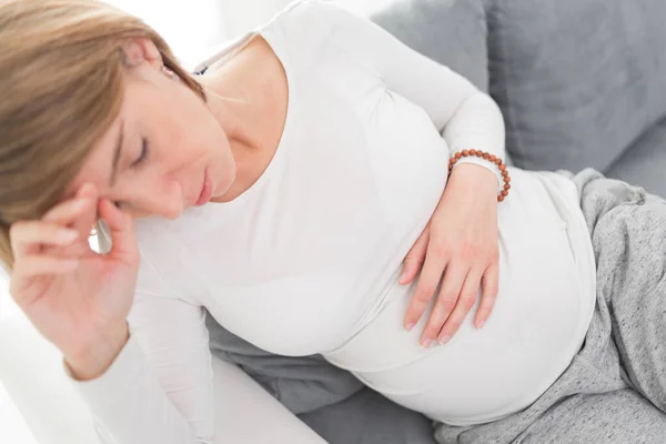 Zwanger vermoeide, vermoeide vrouw met maag- en hoofdproblemen bij h — Stockfoto