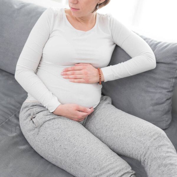 Беременная уставшая измученная женщина с проблемами с желудком дома на
 