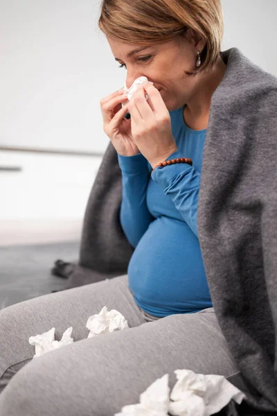 Pregnant woman catching cold, flu, virus, sitting at home on a c