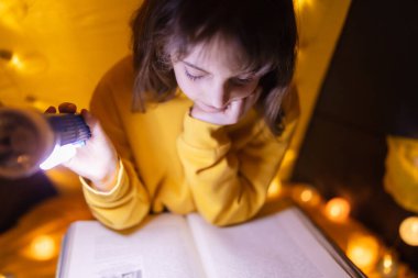Ansiklopedi okuyan küçük bir kız çocuğu, ev yapımı hafif toplarla dolu bir çadırda..