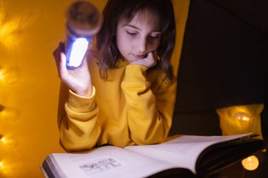 Ansiklopedi okuyan küçük bir kız çocuğu, ev yapımı hafif toplarla dolu bir çadırda..