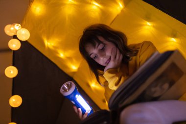 Ansiklopedi okuyan küçük bir kız çocuğu, ev yapımı hafif toplarla dolu bir çadırda..