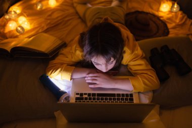 Oturma odasındaki ev yapımı çadırının altında dizüstü bilgisayar kullanan 11 yaşında bir kız..