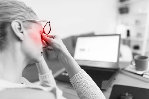 Woman feeling unwell, headache while working on a laptop.