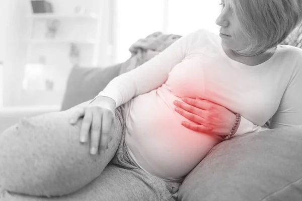 Pregnant tired exhausted woman with stomach issues at home on a couch, being sick.