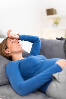 Pregnant tired exhausted woman with stomach and head issues at home on a couch, being sick.