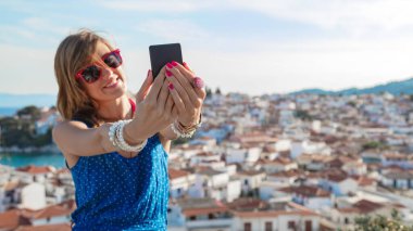 Güzel şehir panoramasının üstünde cep telefonu kullanan genç bir kadın..
