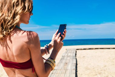 Genç bir kadın tropikal kumsalda cep telefonu kullanıyor..