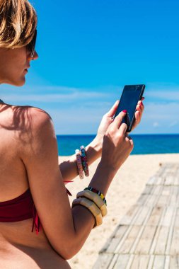 Genç bir kadın tropikal kumsalda cep telefonu kullanıyor..