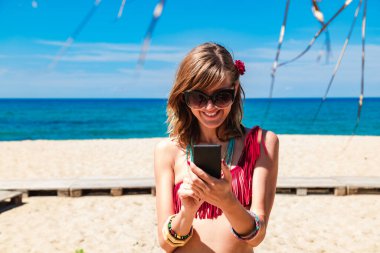 Genç bir kadın tropikal kumsalda cep telefonu kullanıyor..