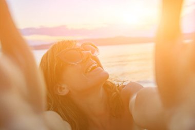 Güneşli bir sahilde selfie çeken gülümseyen kız..