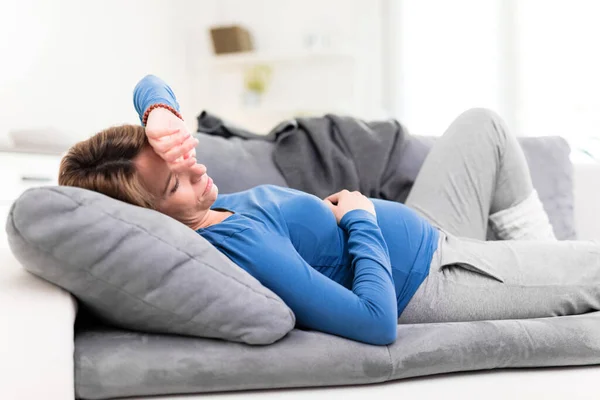 在家里的沙发上有胃部和头部问题的疲倦的怀孕妇女 — 图库照片