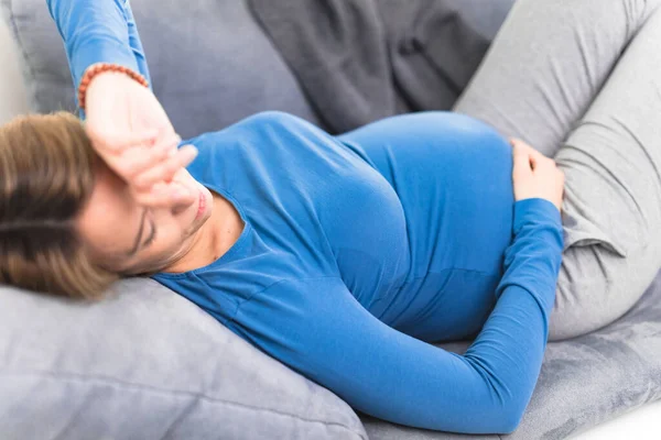 妊娠中の疲れ果てた女性胃と頭の問題を自宅でソファの上に 病気であること — ストック写真