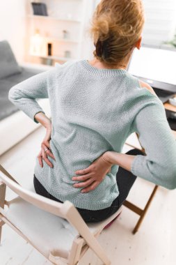 Dizüstü bilgisayarda çalışan ve sırtı, kalçası, omurgası ağrıyan bir kadın..