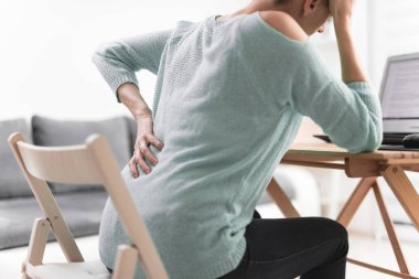 Dizüstü bilgisayarda çalışan ve baş ağrısı çeken bir kadın. Kalça, omurga ağrısı..