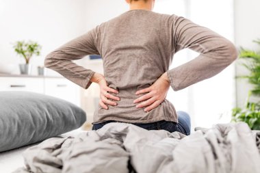 Yatakta uyanan kadın, sabah esnemesi, sırt ve kalça ağrısı..