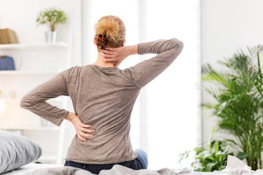 Kadın yatakta uyanıyor, sabah esniyor, sırtı ve boynu ağrıyor..