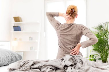 Kadın yatakta uyanıyor, sabah esniyor, sırtı ve boynu ağrıyor..