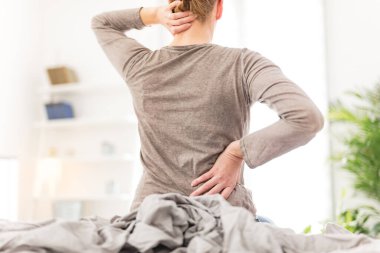 Kadın yatakta uyanıyor, sabah esniyor, sırtı ve boynu ağrıyor..