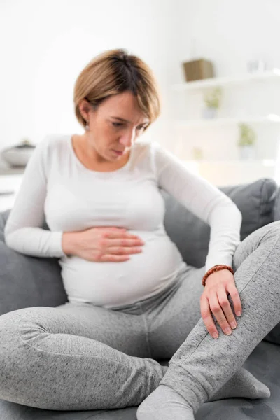 在家里的沙发上 有胃部 腿和疼痛的疲倦的怀孕妇女 — 图库照片