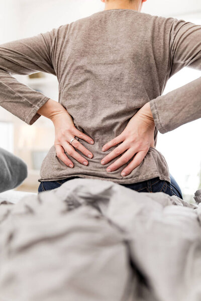 Woman waking up on the bed, morning stretching, pain in the back and hip.