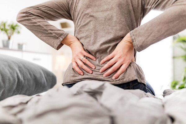 Woman waking up on the bed, morning stretching, pain in the back and hip.