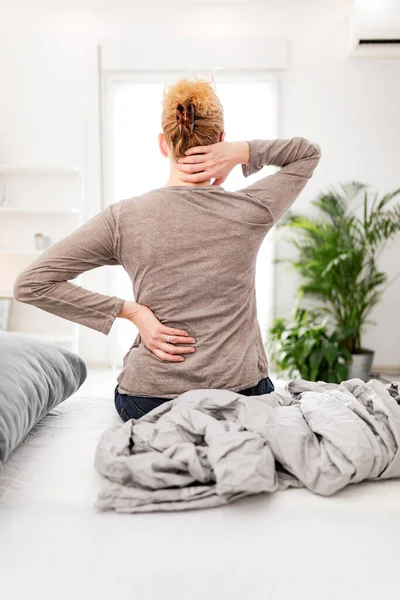 Woman waking up on the bed, morning stretching, pain in the back and neck.