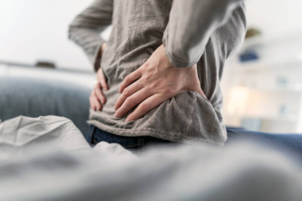 Woman waking up on the bed, morning stretching, pain in the back and hip.