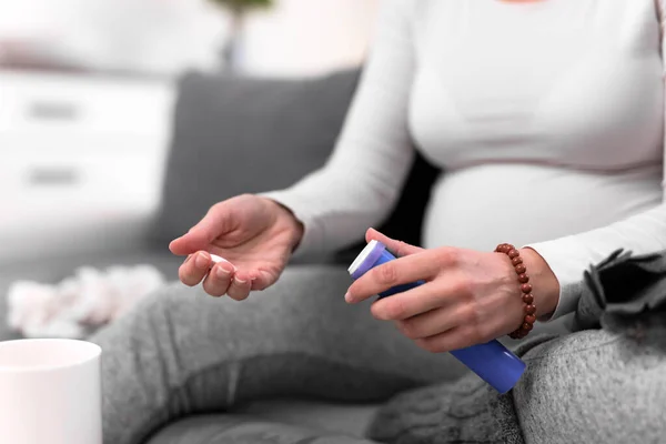 Pregnant woman taking vitamin tablet in a glass of water.