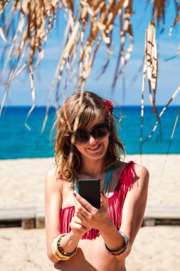 Genç bir kadın tropikal kumsalda cep telefonu kullanıyor..
