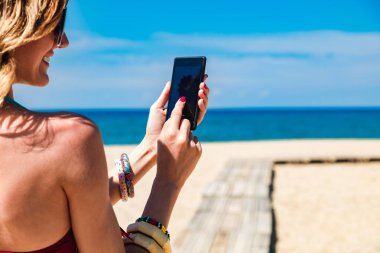 Genç bir kadın tropikal kumsalda cep telefonu kullanıyor..