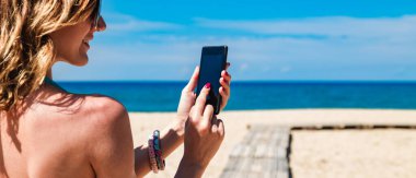 Genç bir kadın tropikal kumsalda cep telefonu kullanıyor..