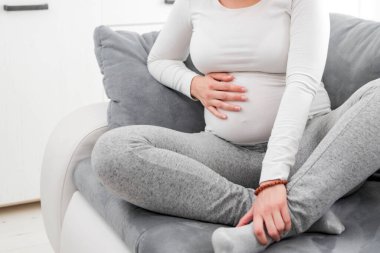 Hamile, yorgun, midesi, bacağı ve ağrısı olan bir kadın, evinde, kanepede hasta..