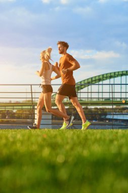 Nehir kenarındaki kentsel çevrede koşan / egzersiz yapan modern kadın ve erkek.