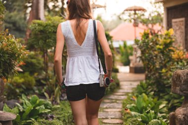 Arka planda güneş ışığı olan parkta retro kameralı bir kadının silueti..