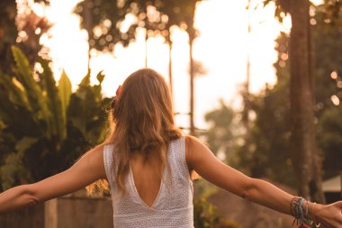 Arka planda turuncu güneş ışığıyla havada el ele tutuşan bir kadın..