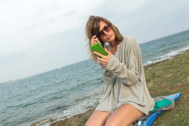 Sahilde cep telefonu kullanan genç kadın.