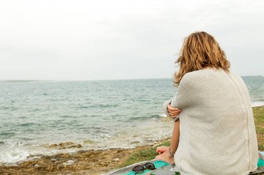 Cep telefonu olan genç bir kadın sahilde oturuyor..