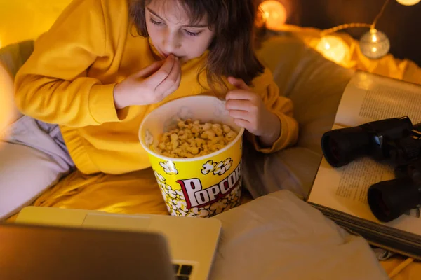 11岁的小女孩在客厅里的自制帐篷下使用笔记本电脑 吃爆米花 — 图库照片