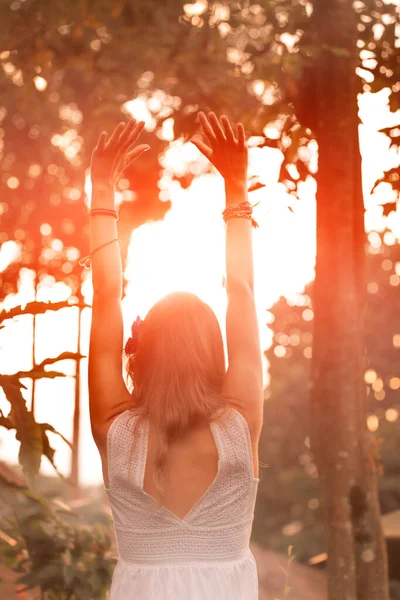 Woman holding hands in the air with orange sunlight in the background.